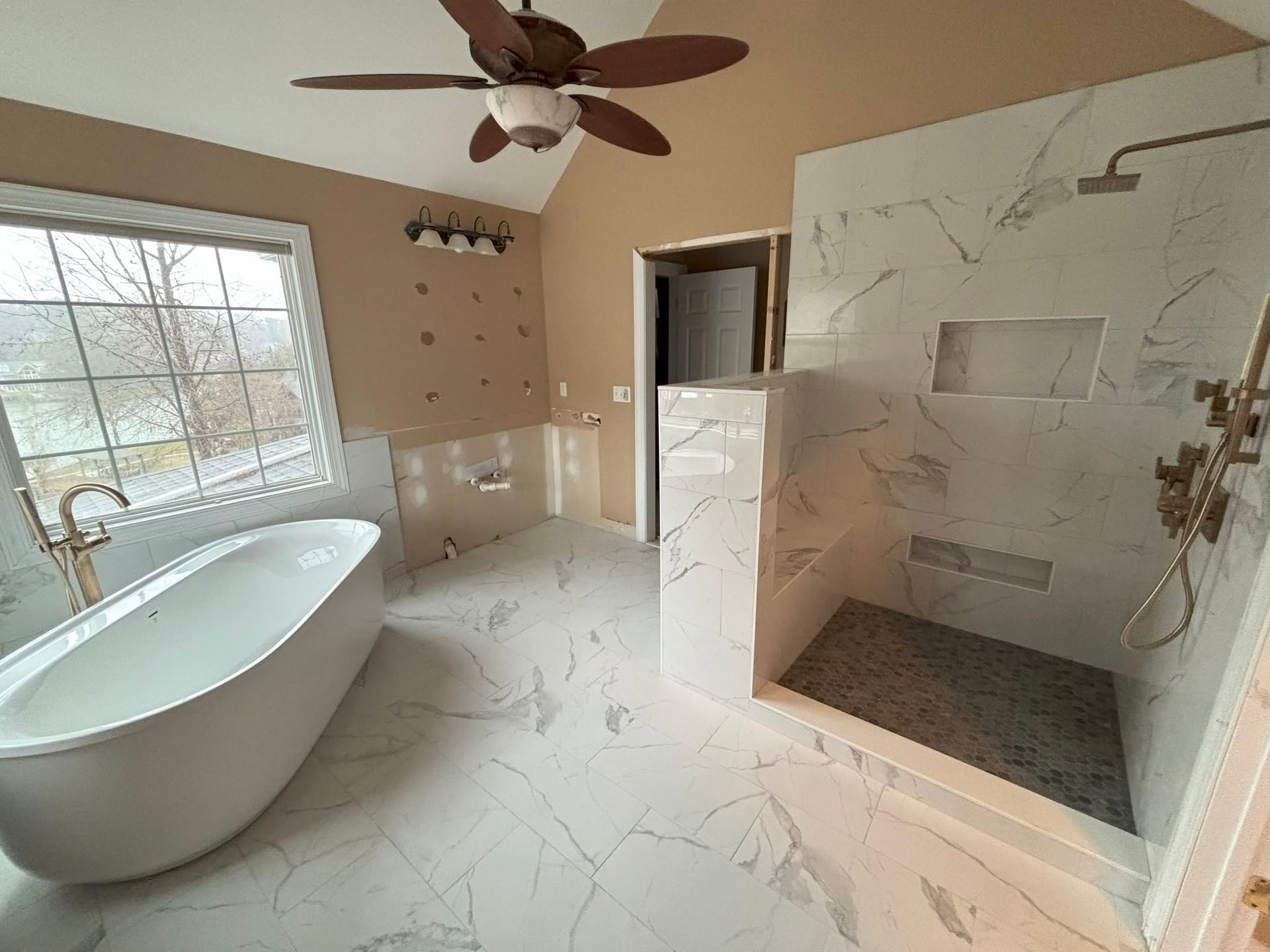 Modern bathroom with freestanding tub, marble shower, window, and ceiling fan