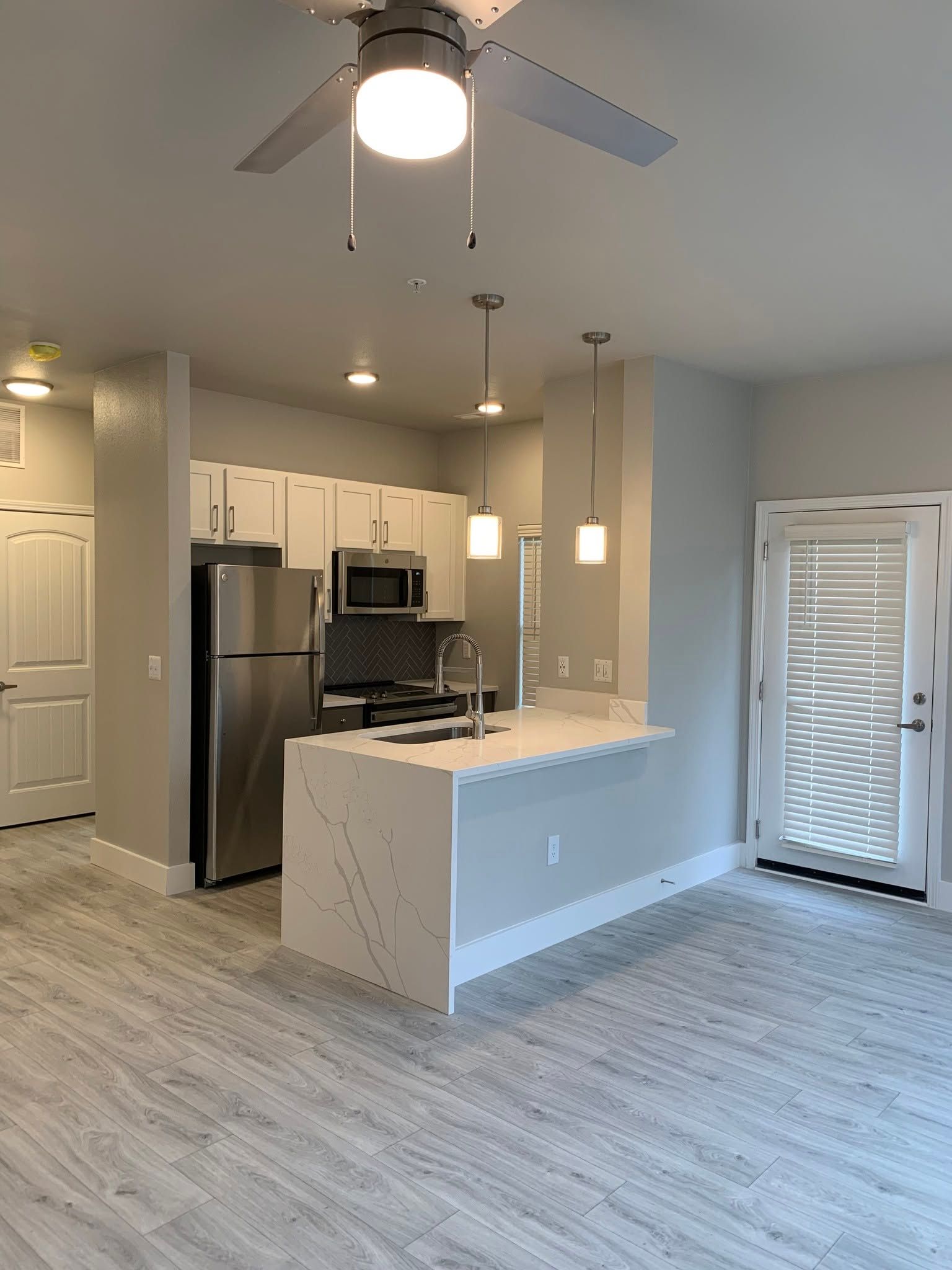 Empty modern kitchen and living area with stainless appliances, white cabinets, and ceiling fan