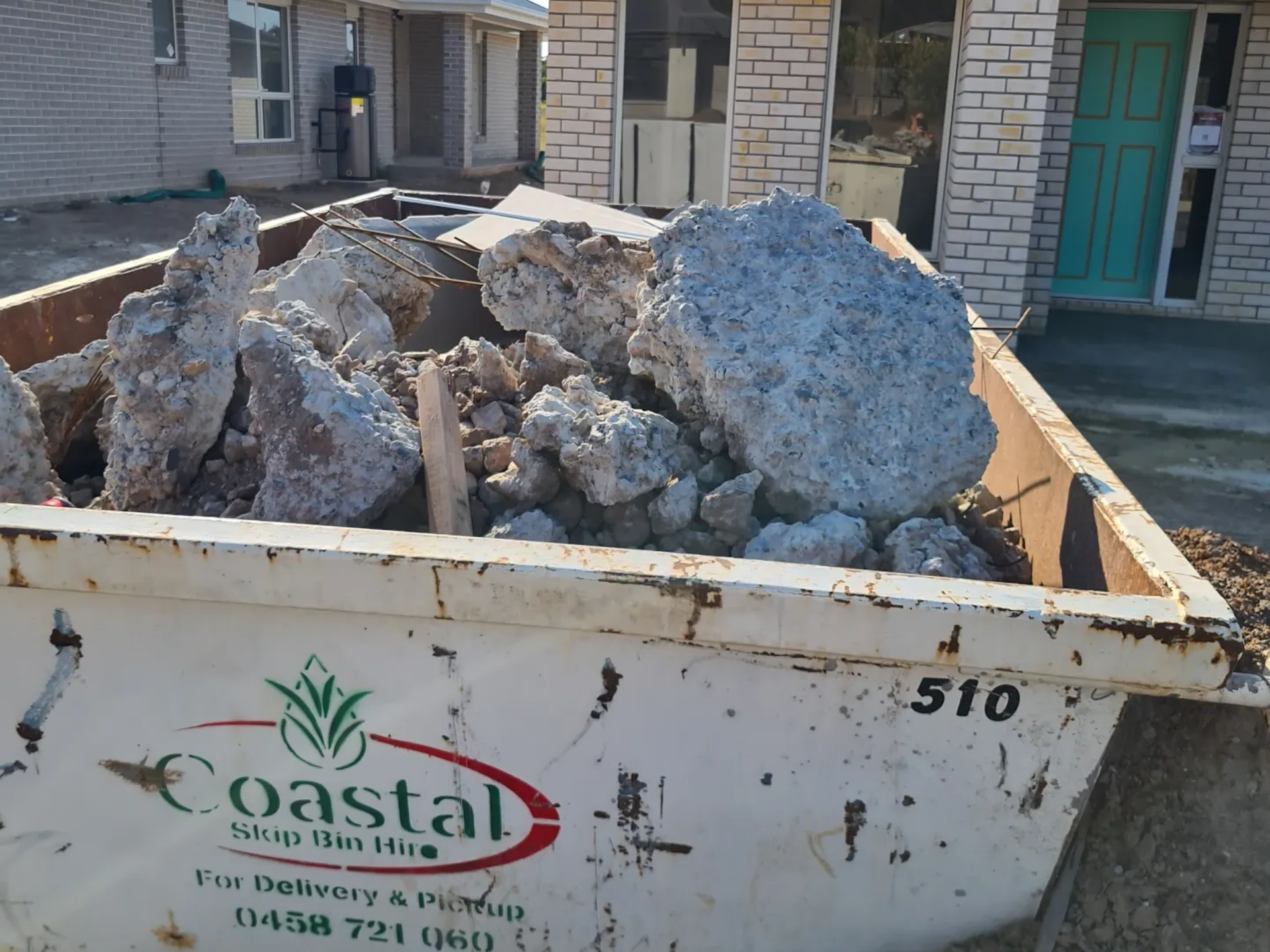 A skip bin overflowing with rubble in front of a house. 