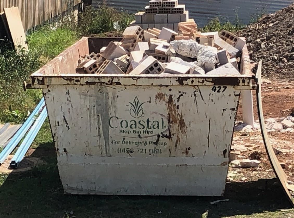 White Dumpster Full of Broken Concrete Blocks on a Dirt Lot Beside a Wall — Coastal Skip Bin Hire In Craignish, QLD