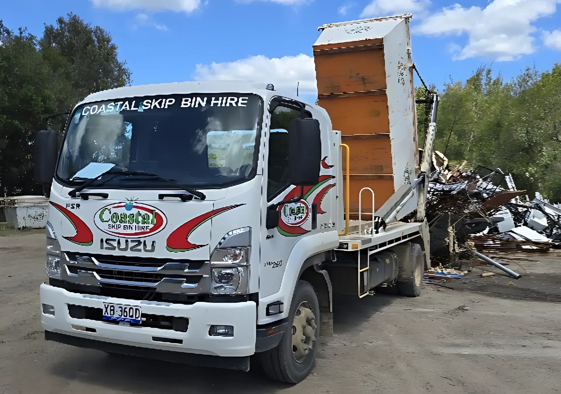 White Coastal Skip Bin Hire truck with an open bin, near a pile of metal scraps.  Coastal Skip Bin Hire In Craignish, QLD