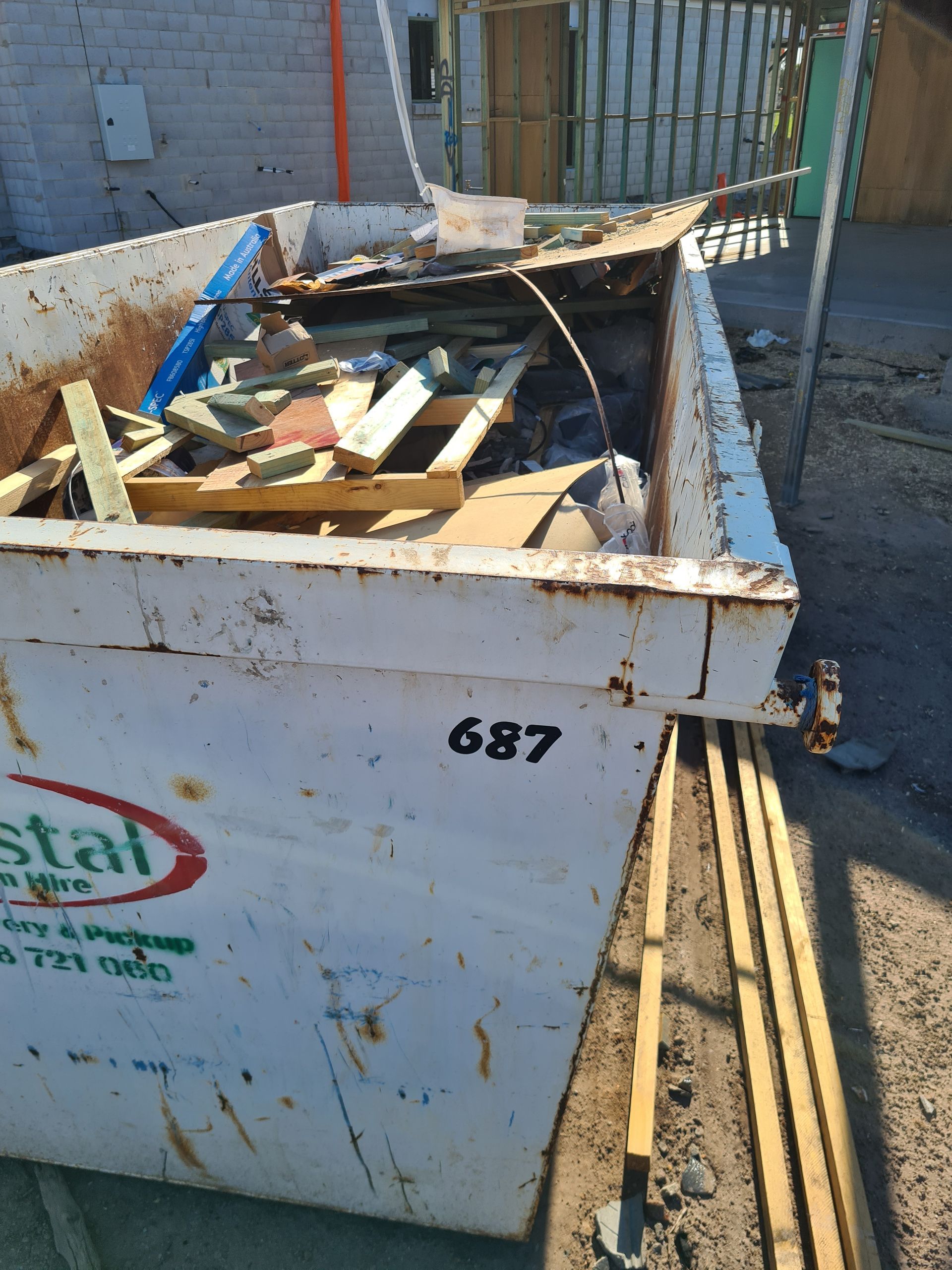 Green dumpster filled with yard waste, including branches, leaves, and green plants, on a street. — Coastal Skip Bin Hire In Point Vernon, QLD