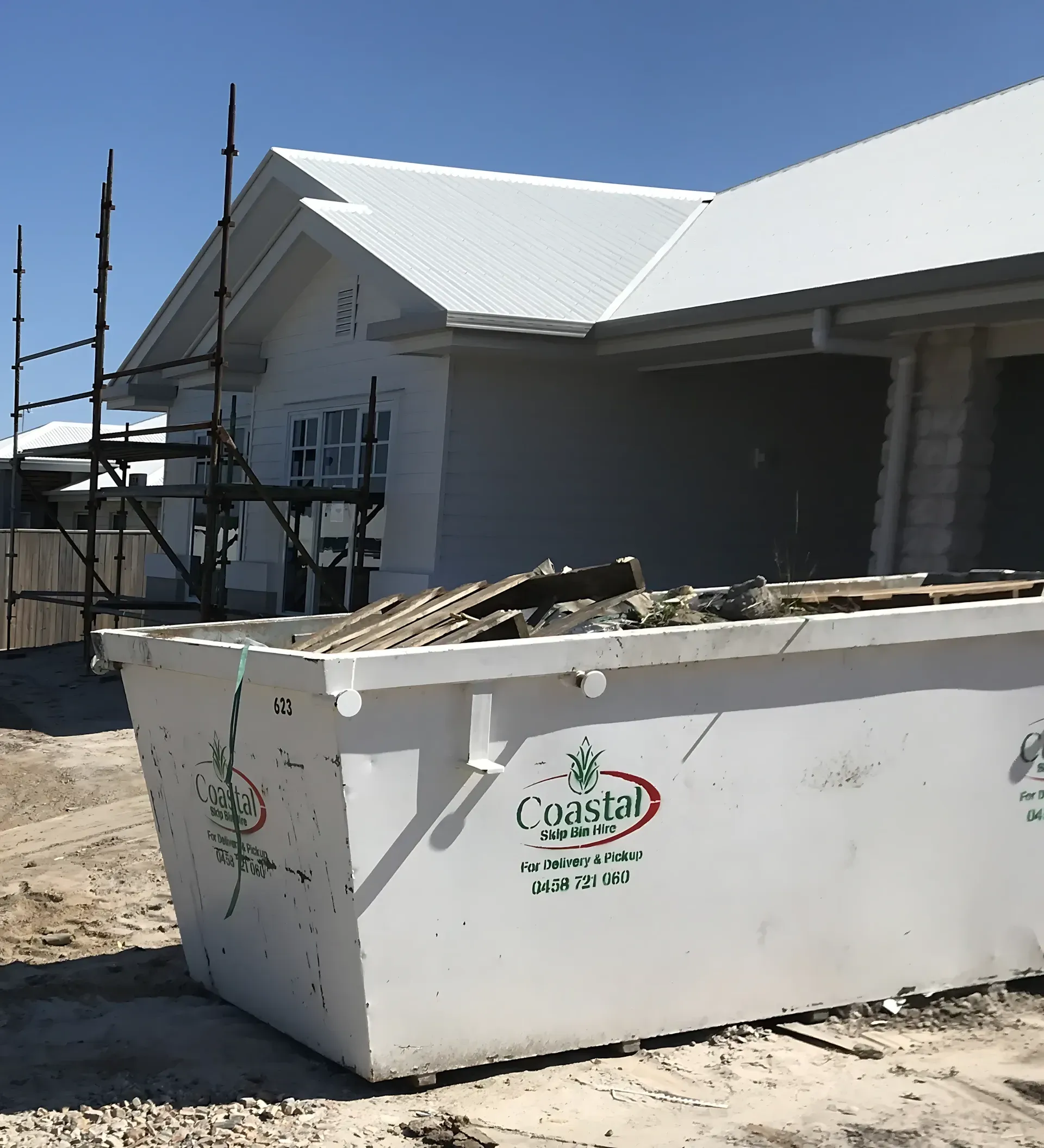 White dumpster at construction site; white house with scaffolding in the background — Coastal Skip Bin Hire In Maryborough, QLD