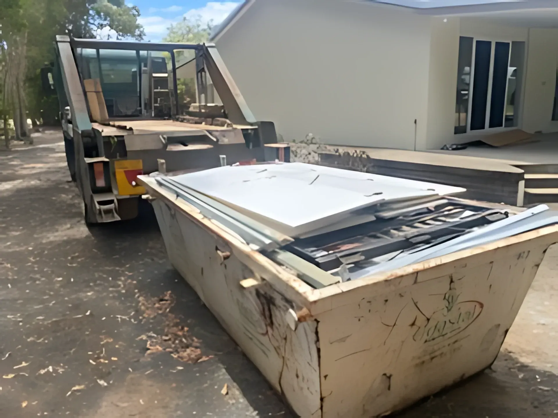 Dumpster filled with construction debris, being loaded by a truck in front of a house. — Coastal Skip Bin Hire In Urraween, QLD