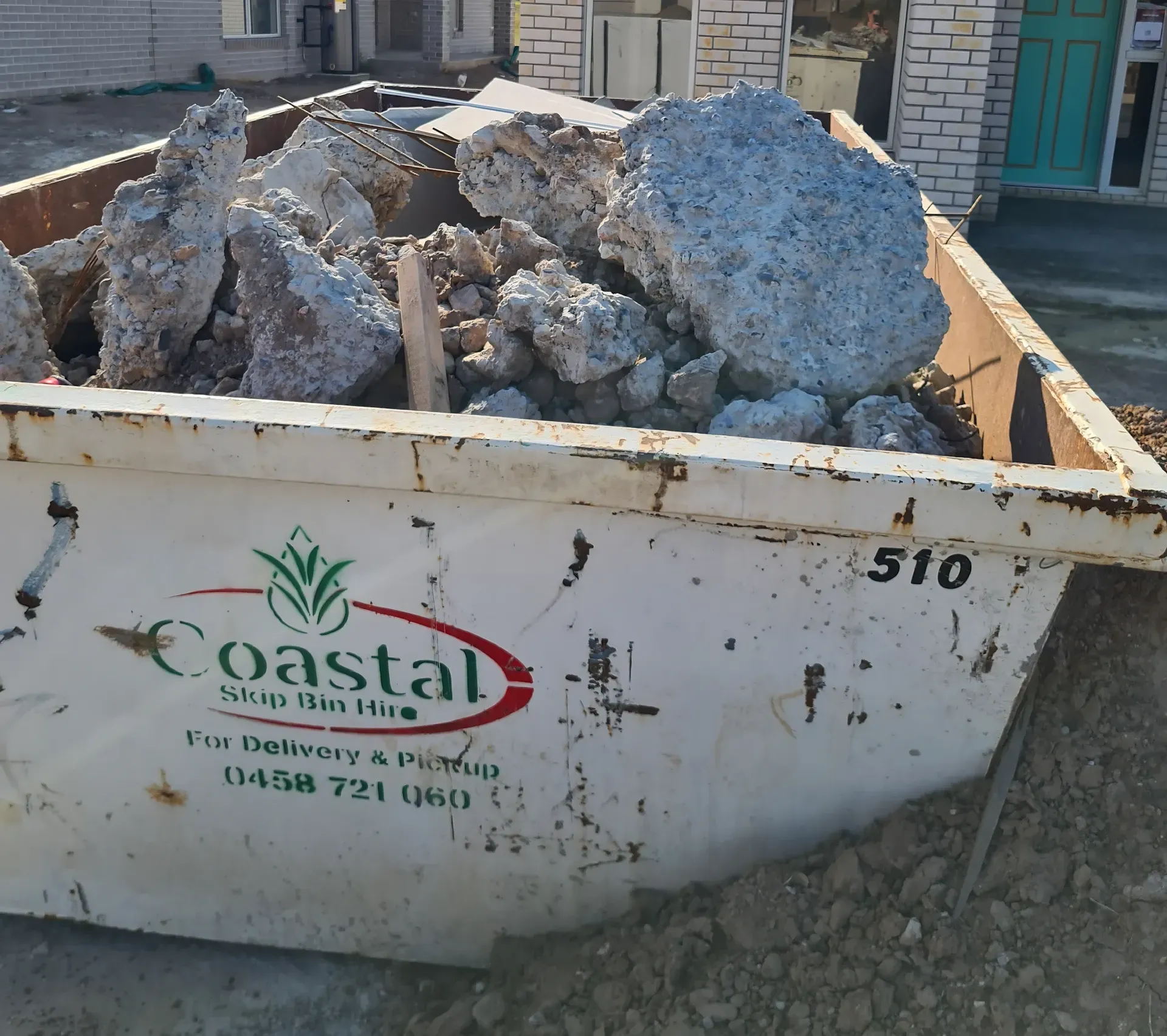 A white dumpster filled with large concrete chunks, with a Coastal Skip logo on the side.  — Coastal Skip Bin Hire In Fraser Coast, QLD