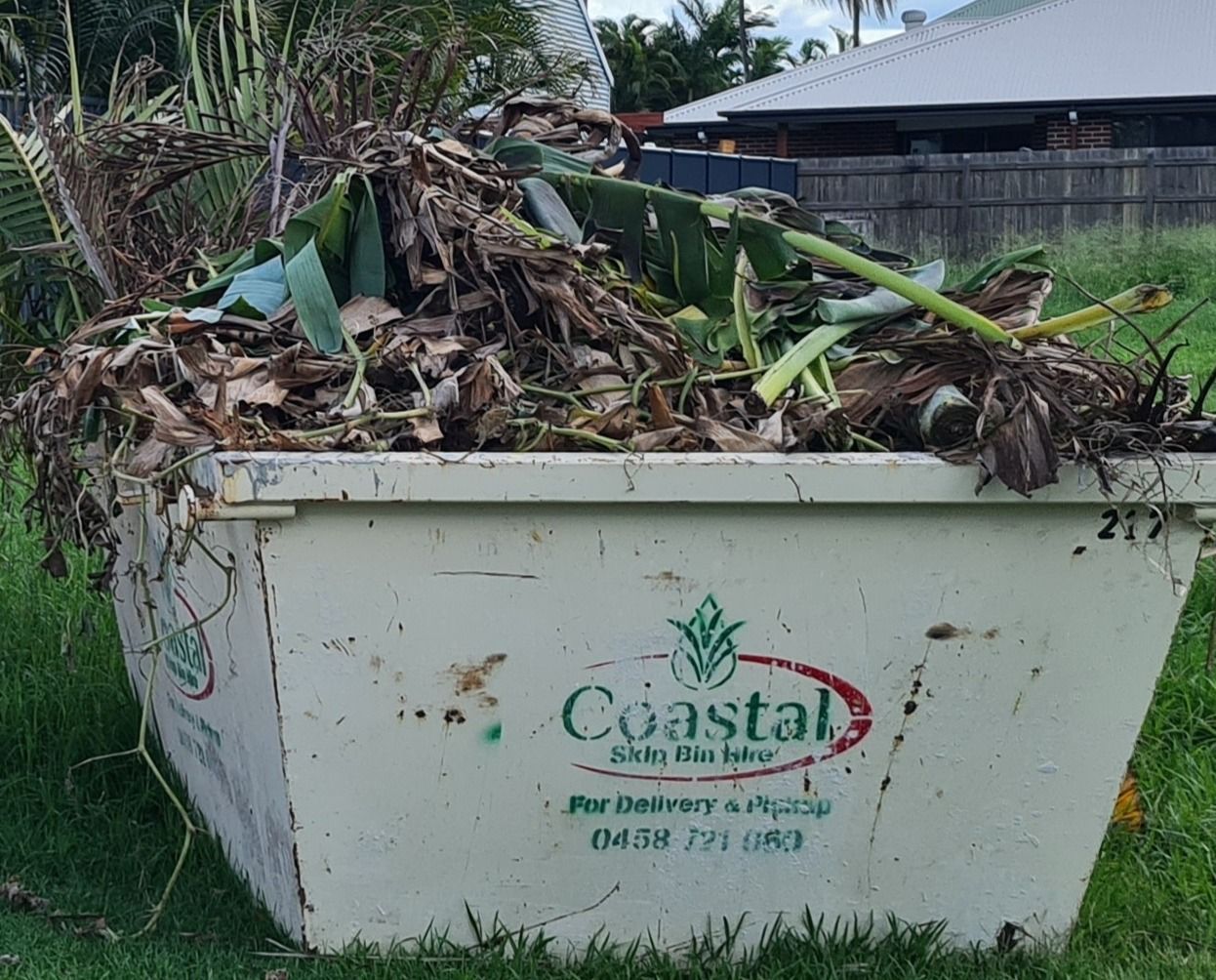 A full skip bin filled with green and brown garden waste; bin is branded 