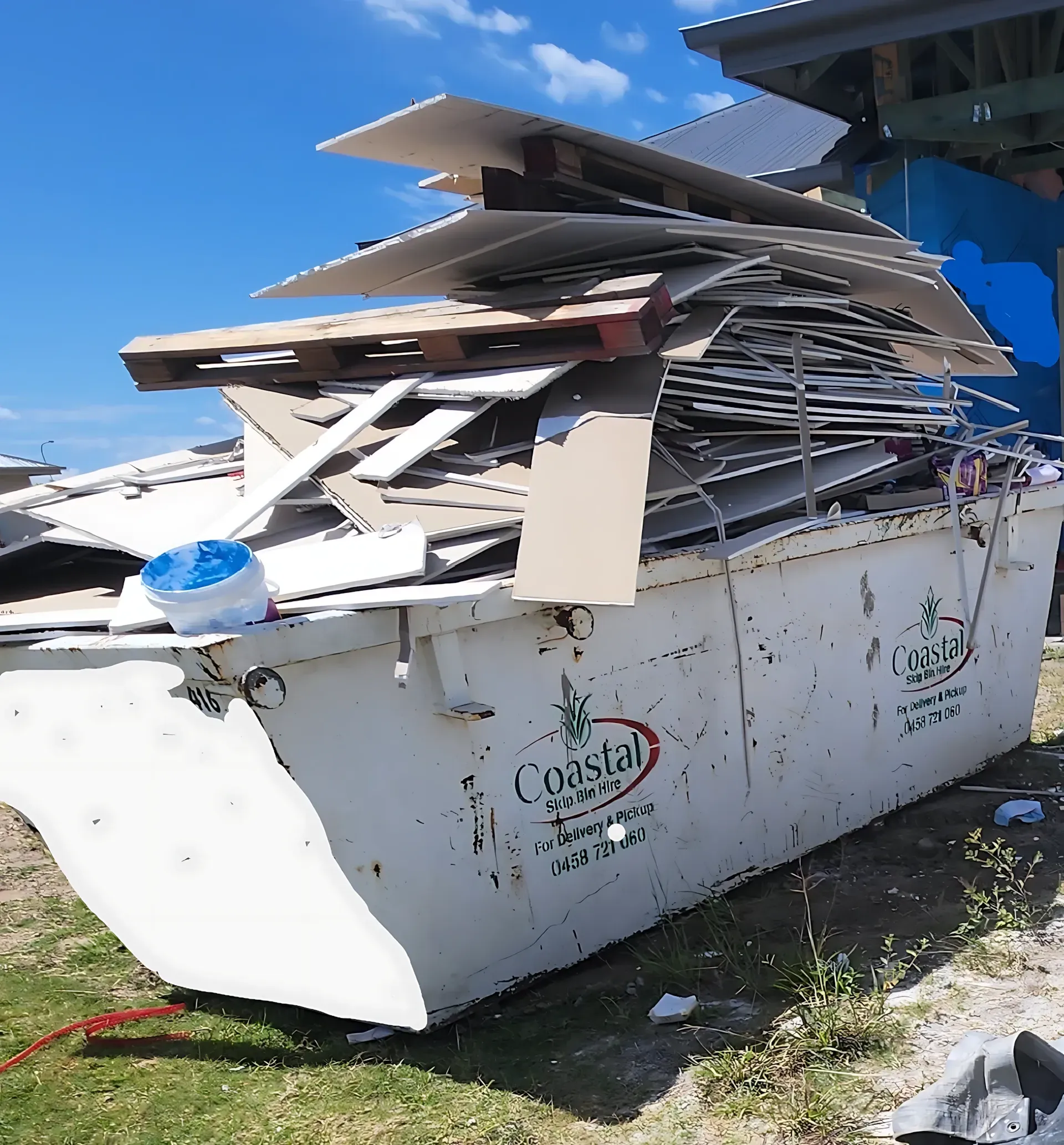 A white Coastal waste dumpster overflowing with construction debris under a blue sky. — Coastal Skip Bin Hire In Eli Waters, QLD