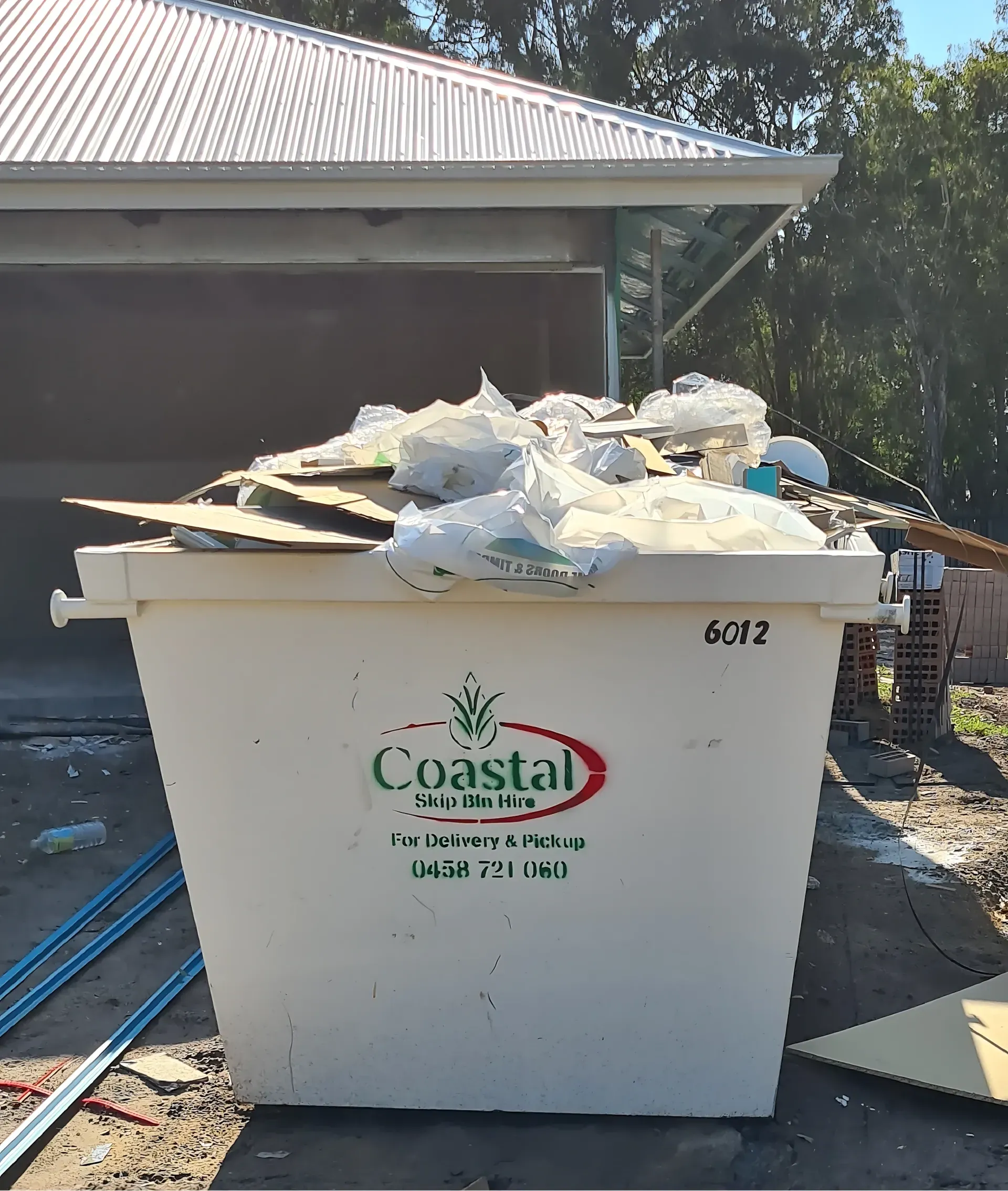 White Coastal Skip Bins container overflowing with debris in front of a building. — Coastal Skip Bin Hire In Maryborough, QLD