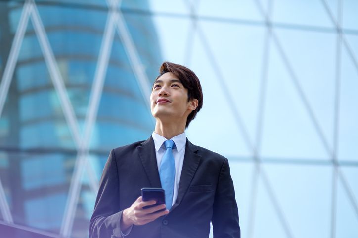 A man in a suit and tie is looking up at the sky while holding a cell phone.