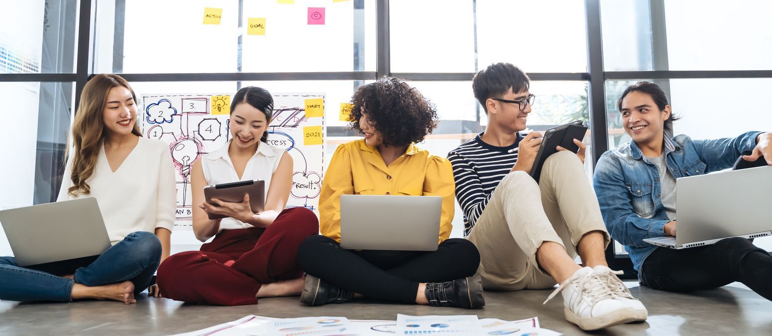 A group of people are sitting on the floor with laptops.