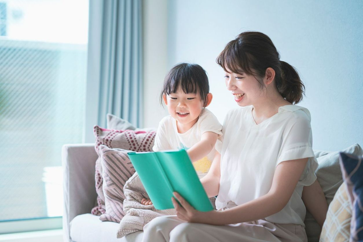 A woman and a little girl are sitting on a couch reading a book.