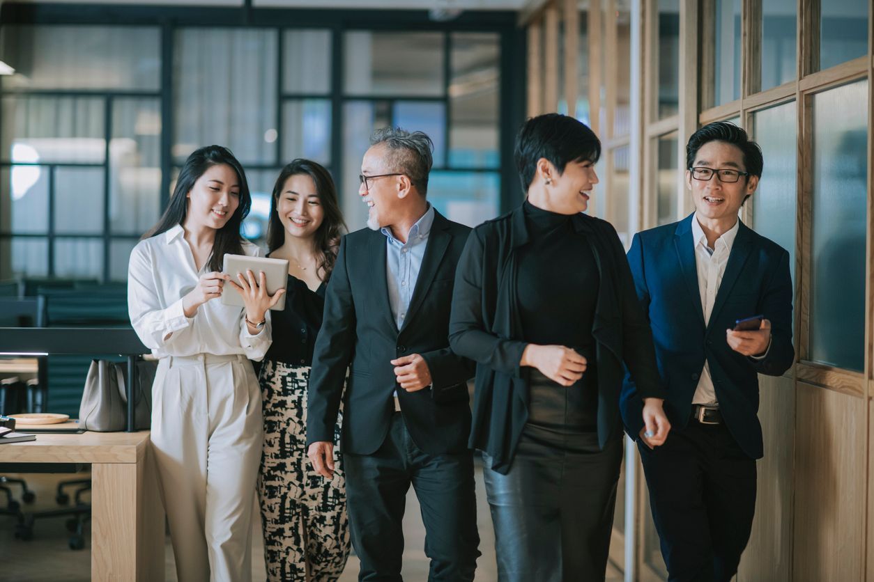 A group of business people are walking down a hallway in an office.