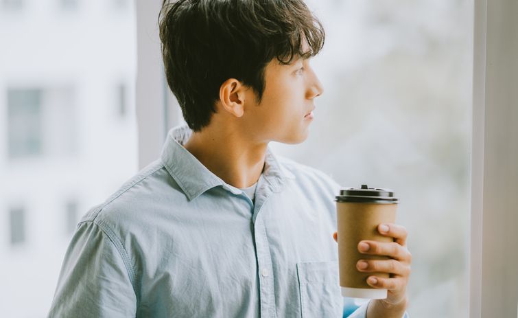 A man is holding a cup of coffee and looking out of a window.