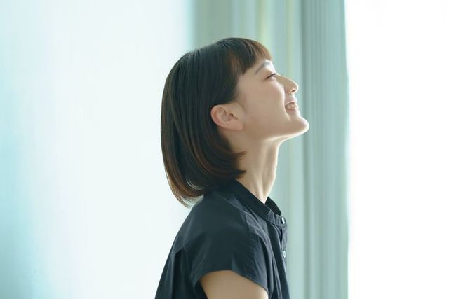 A woman is looking up at the sky while standing in front of a window.