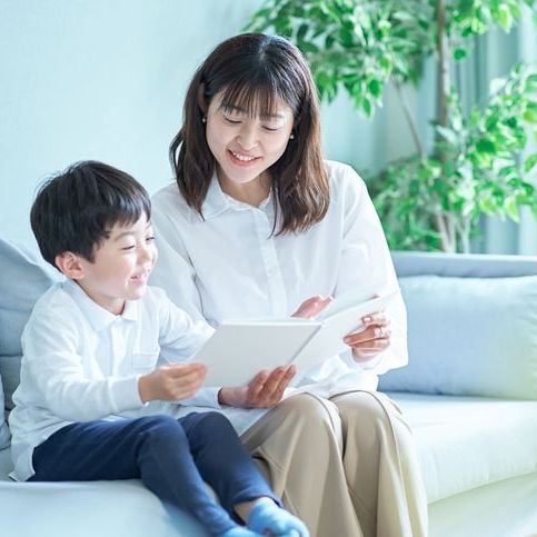 A woman and a child are sitting on a couch looking at a tablet.