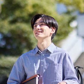 A young man in a blue shirt is holding a book and smiling.