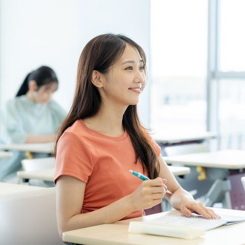 A woman is sitting at a desk in a classroom holding a pen.