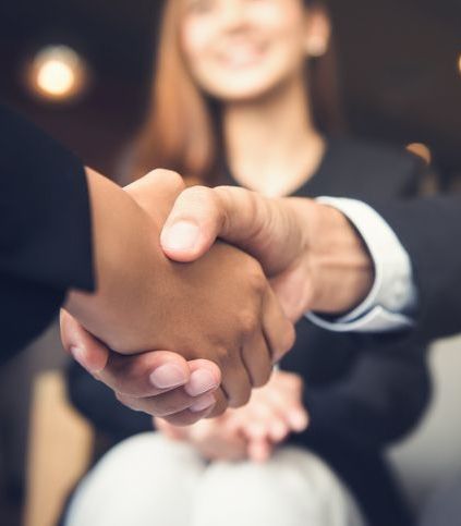 A man and woman shaking hands with a woman in the background