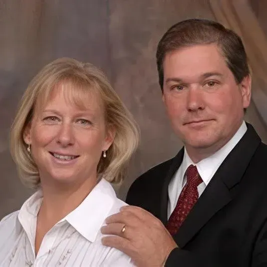 Couple posing for a portrait; woman smiling, man in suit with hand on her shoulder.