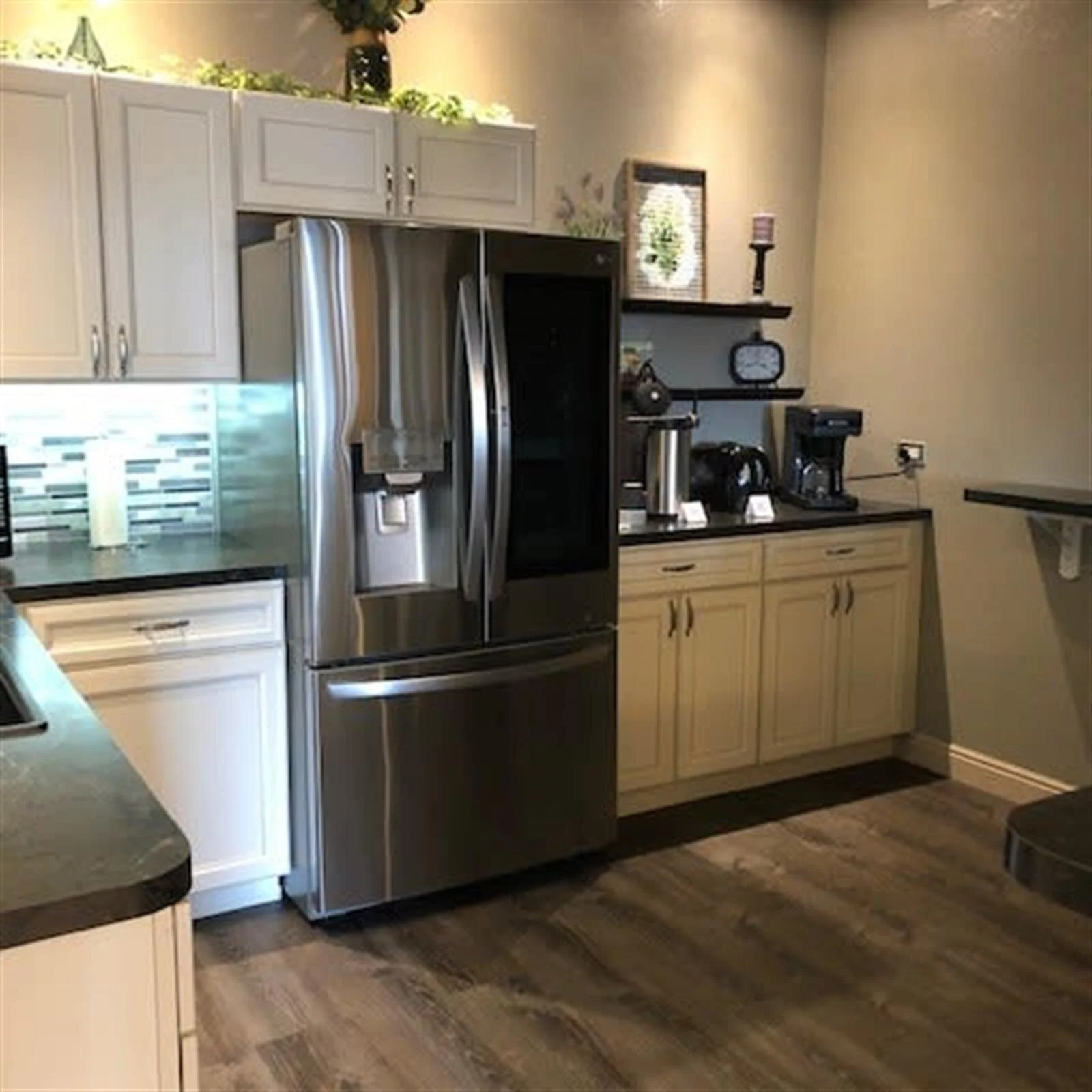 Modern kitchen with stainless steel fridge, light cabinets, and coffee station.