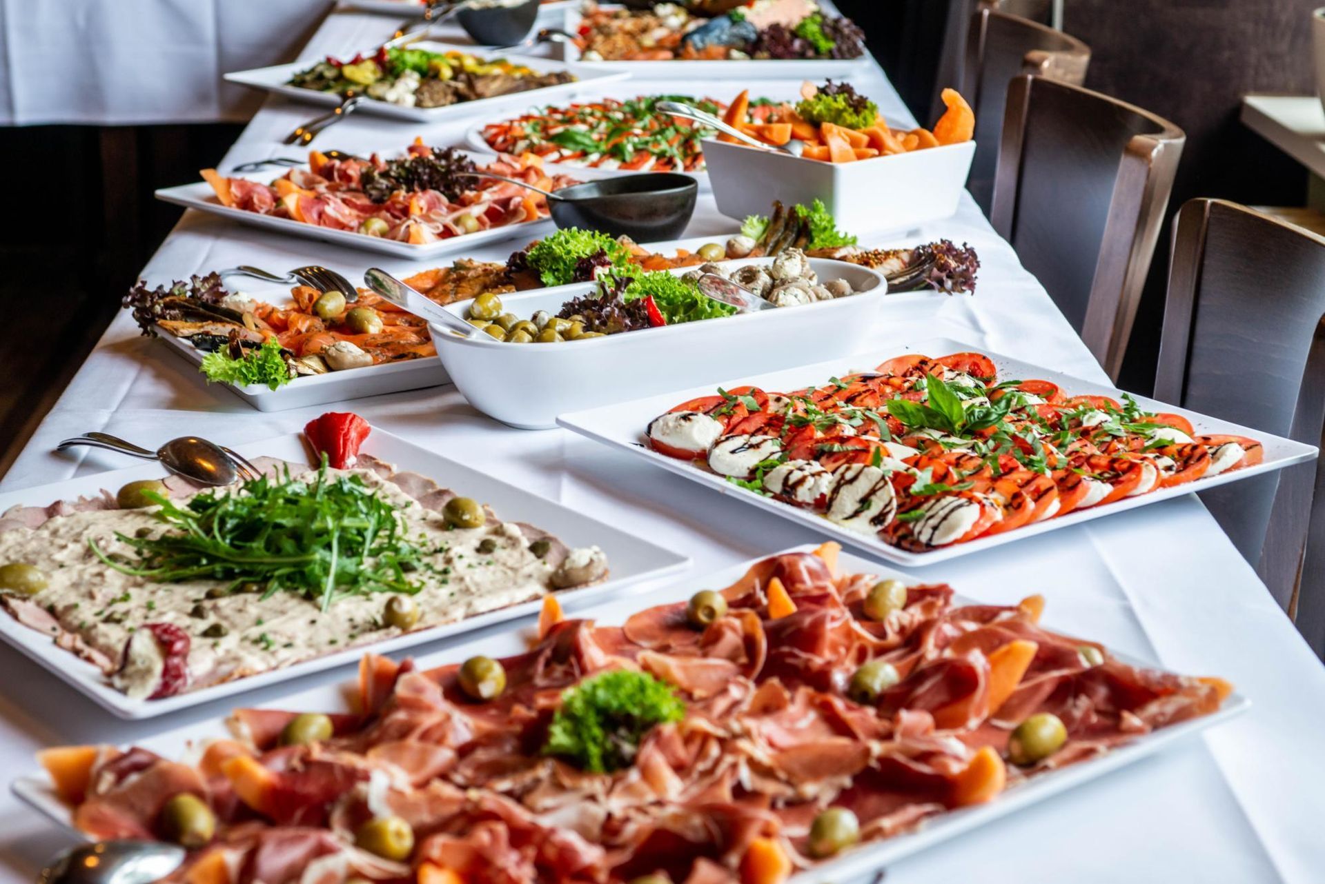Long buffet table with assorted pizzas and flatbreads on white platters in a dining room