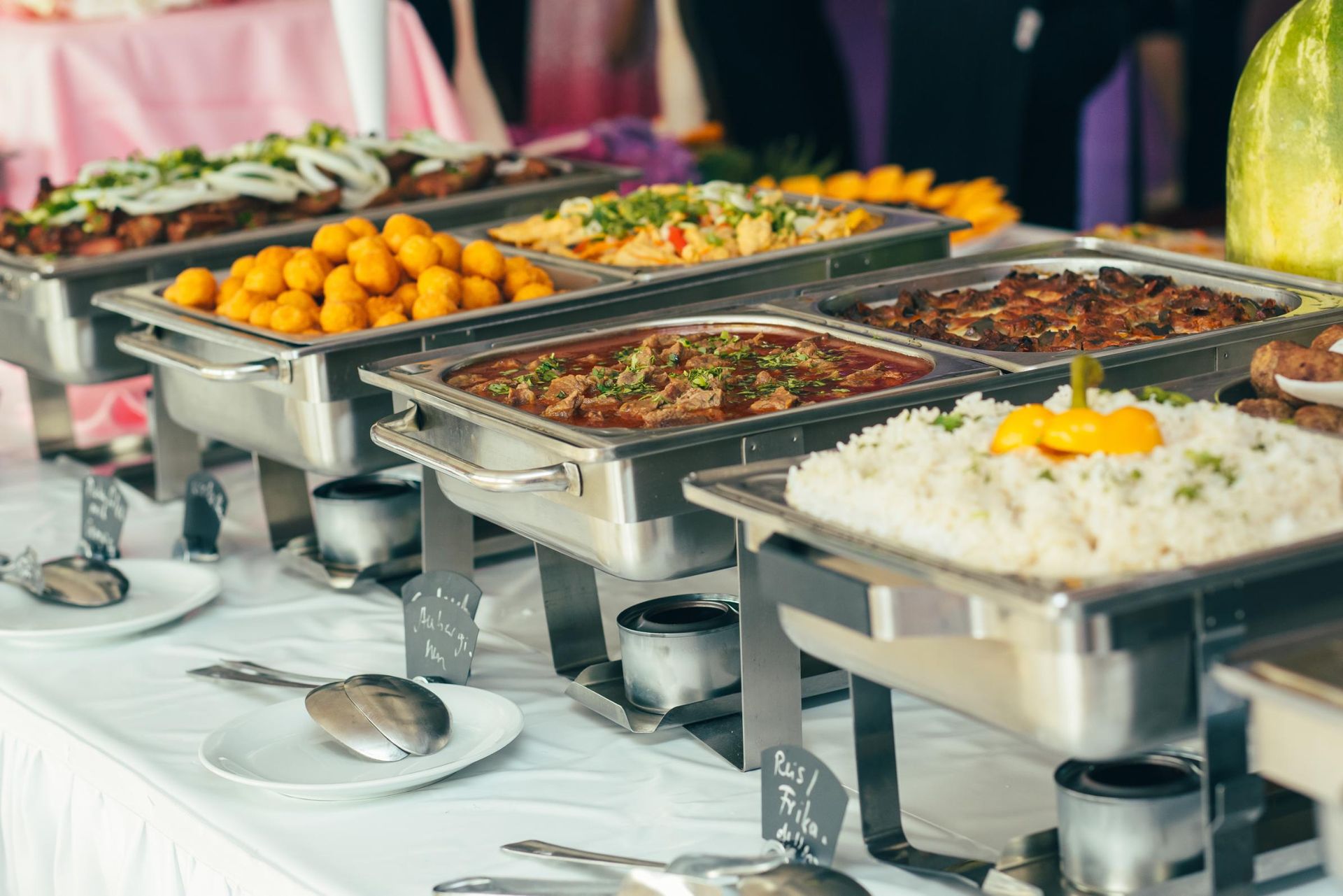 Buffet table with stainless steel trays of assorted dishes, including rice, vegetables, and fried snacks