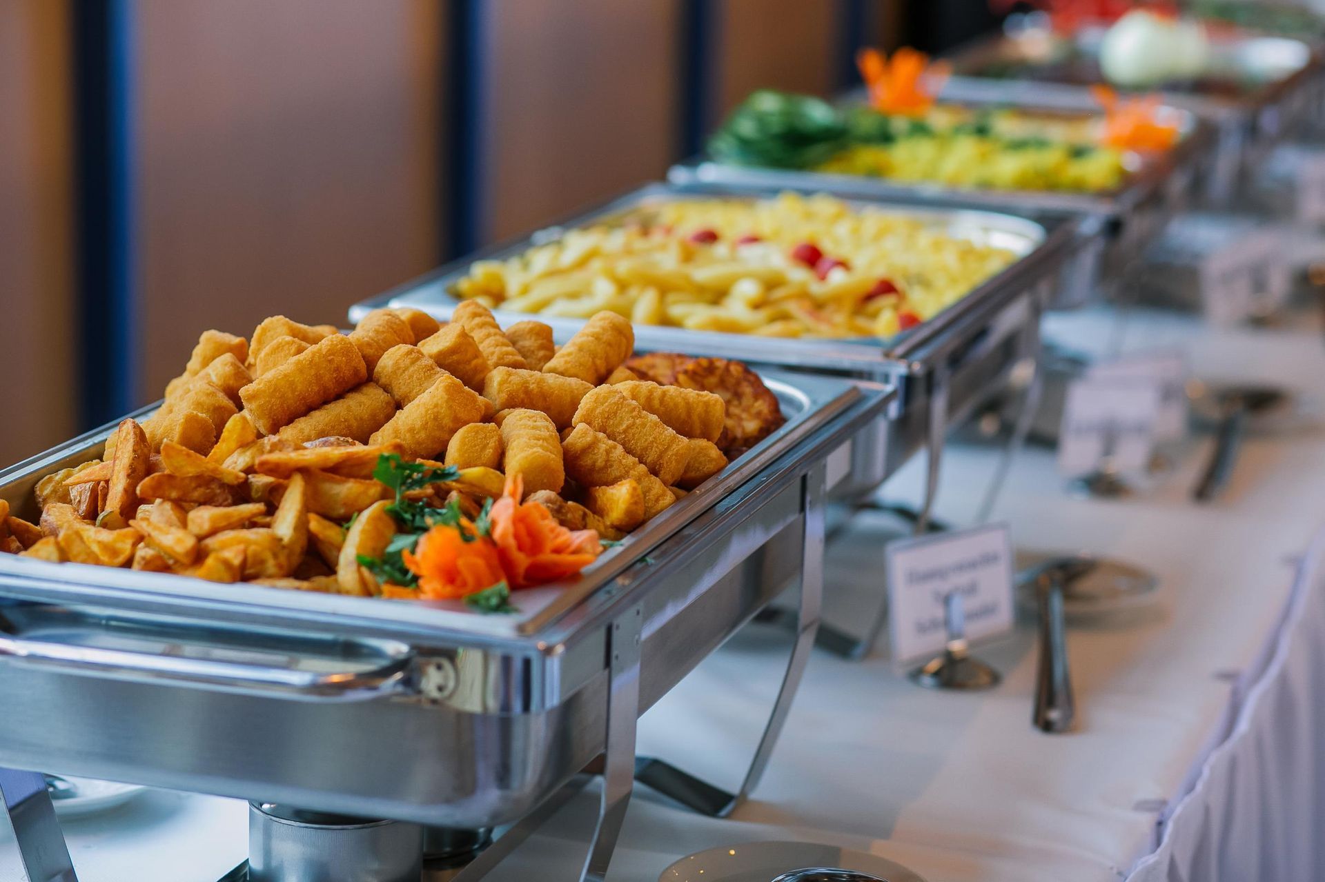 Buffet table with trays of assorted hot dishes and vegetables in a dining hall
