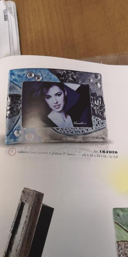 Una cornice con l'immagine di una donna è posta su una superficie bianca con del testo. La cornice è blu, argento e nera.