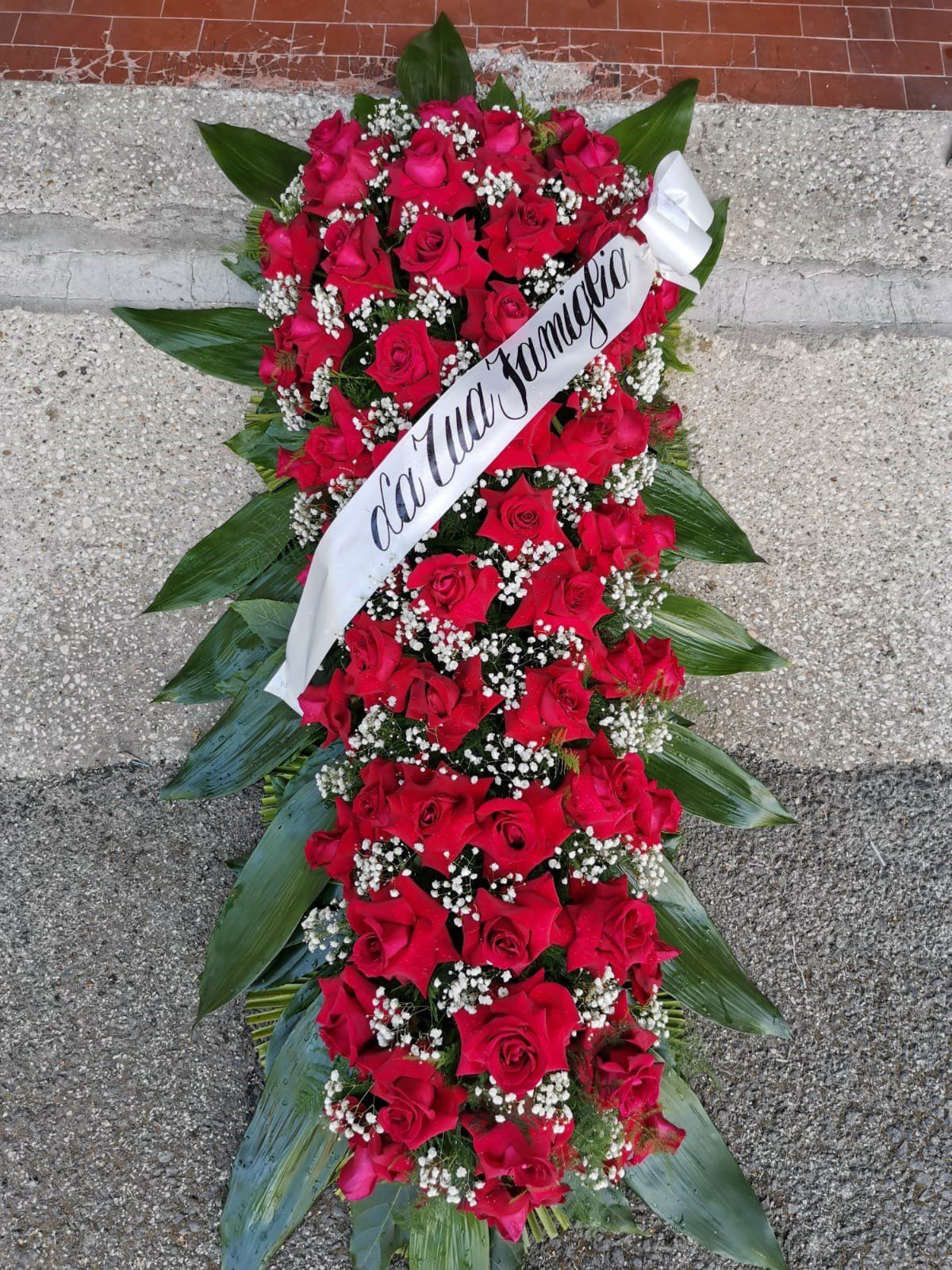 Composizione funebre con rose rosse e nastro bianco