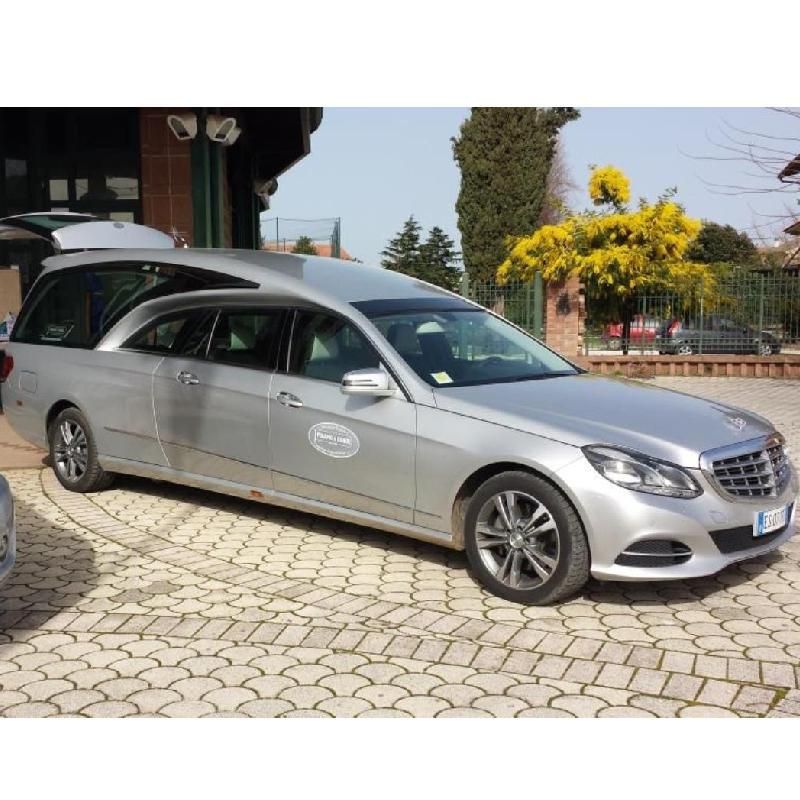 Carro funebre argentato parcheggiato su un marciapiede