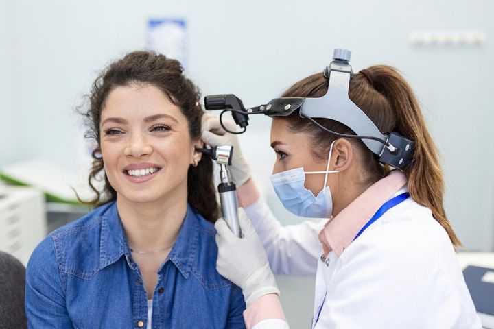 Doctor examining a patient's ear with an otoscope in a clinic. Both are smiling.
