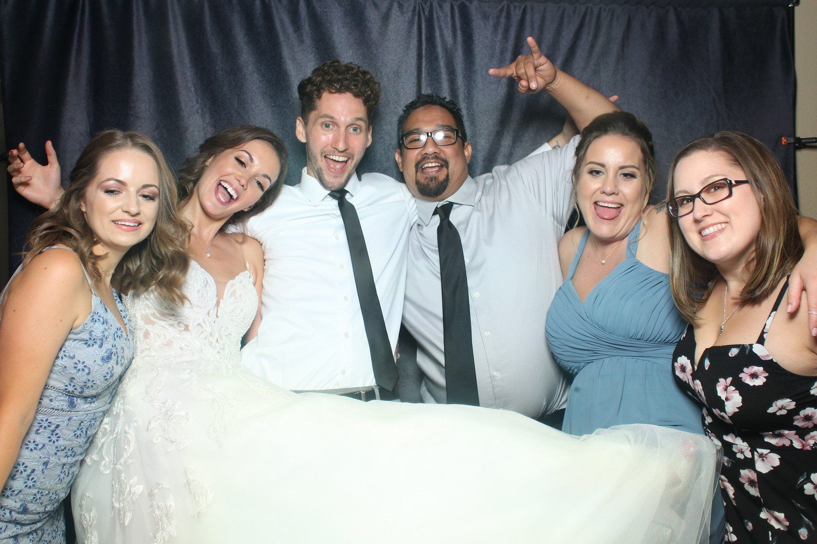 Group of six people smiling and posing in a photo booth at a wedding.