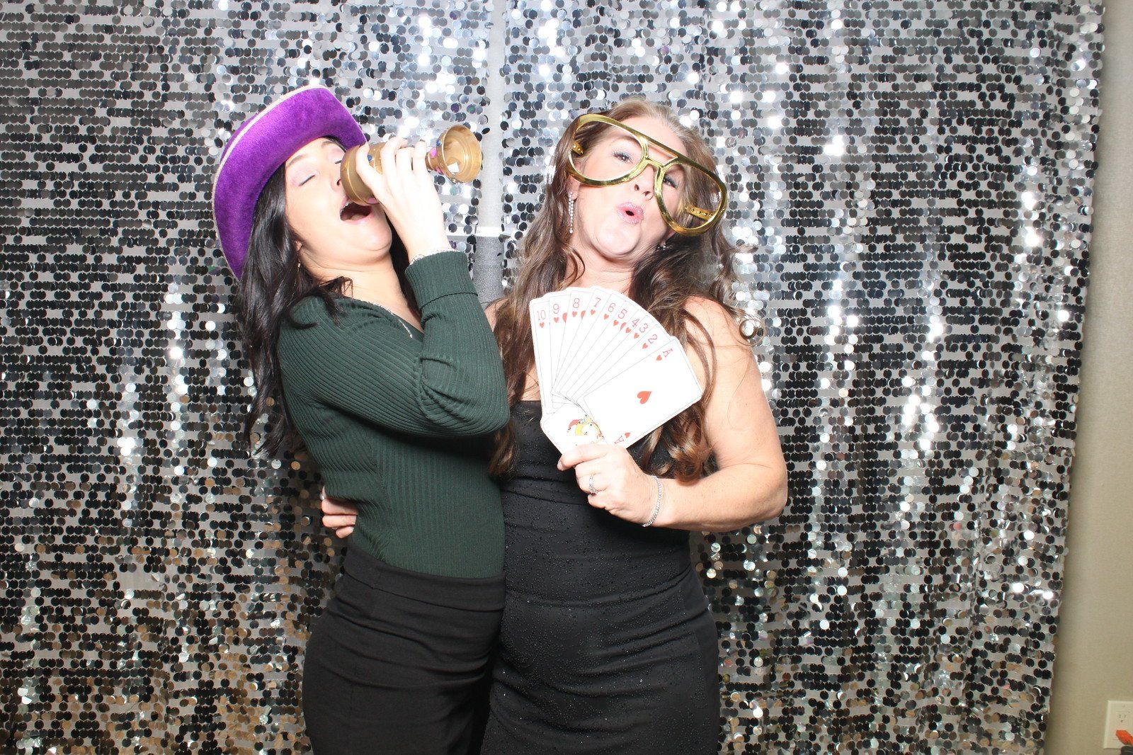 Four people posing for a photo booth with festive hats and props against a pink backdrop, showing joyful expressions.