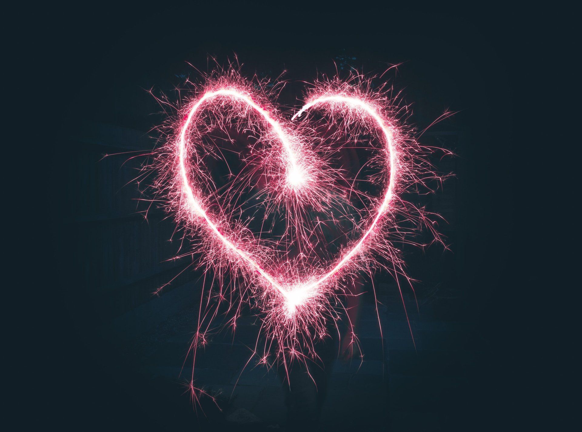 Pink sparkler drawing a heart shape against a dark background.