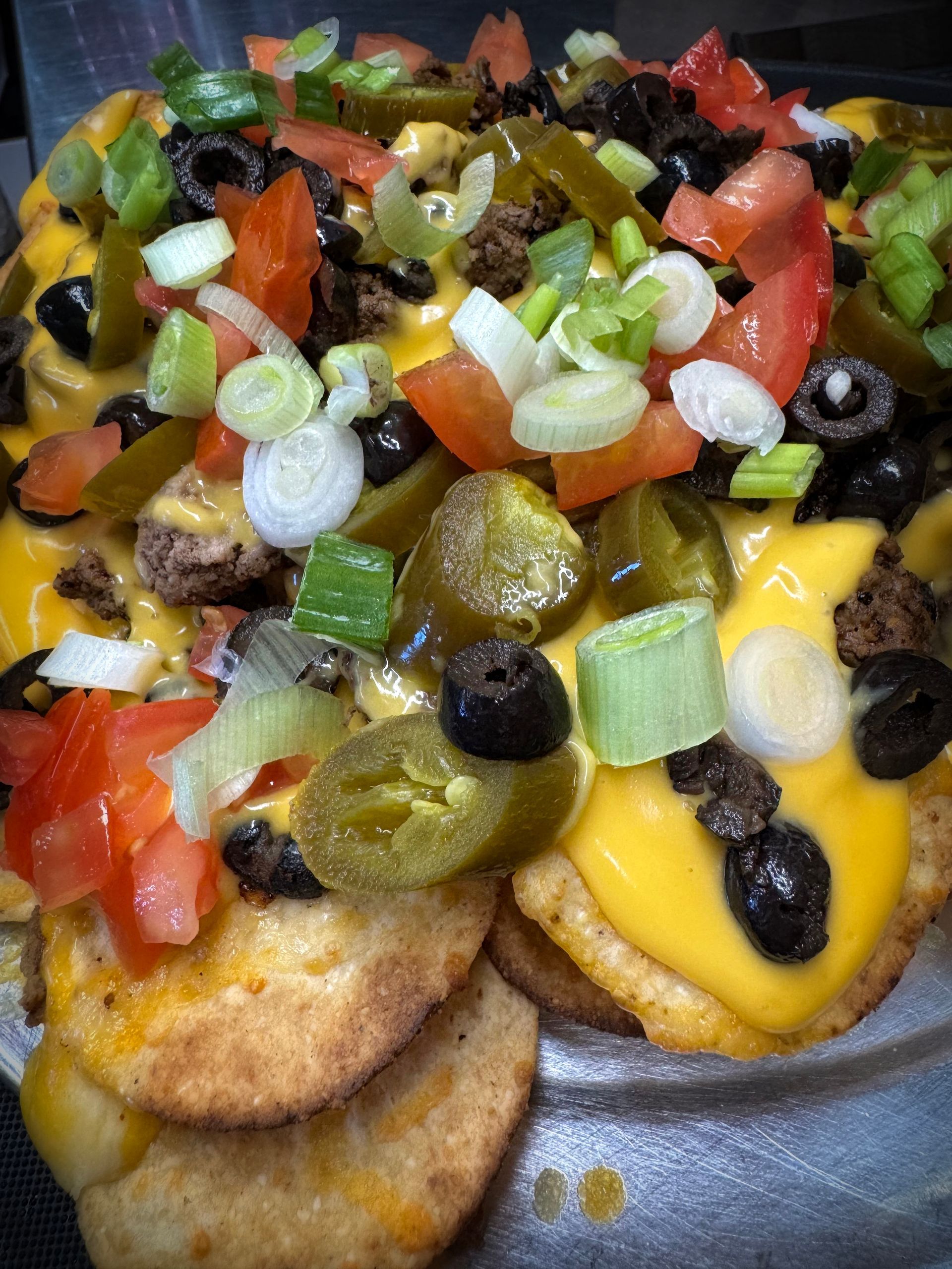 Nachos with melted yellow cheese, jalapenos, olives, tomatoes, and green onions.