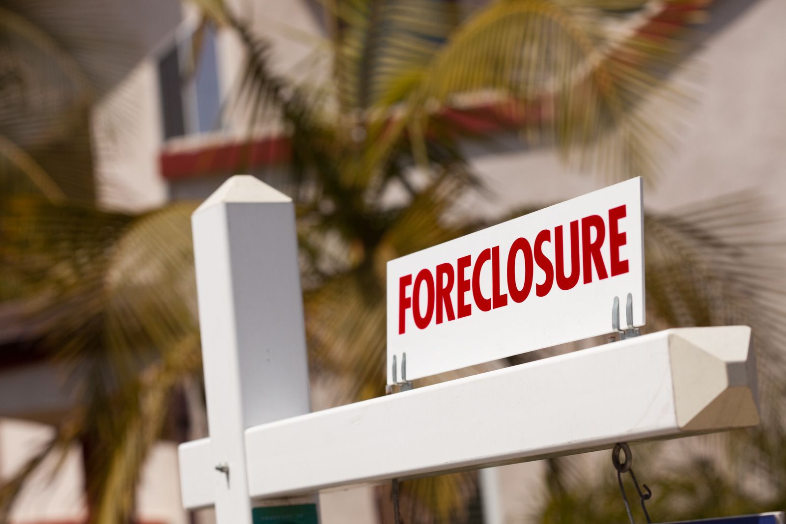 White foreclosure sign on a house post with blurred palm trees in the background