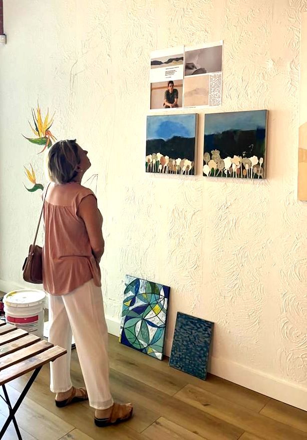 A woman is standing in a room looking at paintings on a wall at the coffee culture in Fort lauderdale