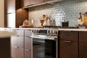 Modern kitchen with marble island, black pendant lights, wood cabinets, and a vase of greenery