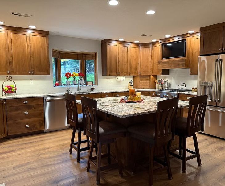 Modern kitchen with wood cabinets, granite island, stainless appliances, and a dining table by a window.