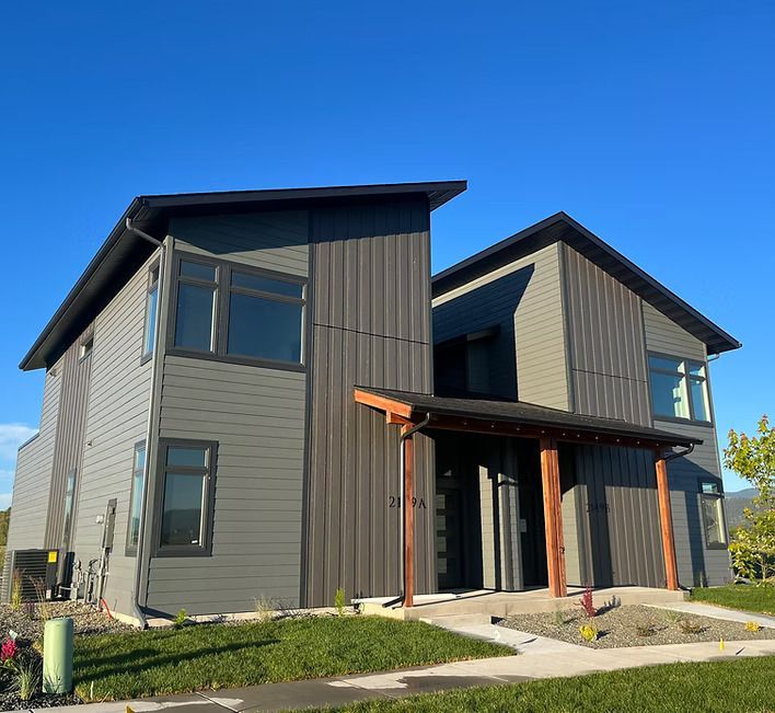 Modern two-story house exterior with gray siding, black trim, and a small front porch under a clear blue sky