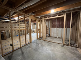 Basement under construction with exposed wooden framing, insulation, and concrete floor under ceiling beams