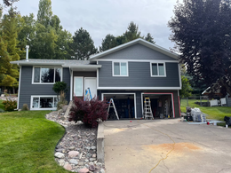 Gray split-level house with two-car garage, driveway, and front lawn under trees