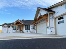 Newly built house exterior with white siding, wooden trim, and a large garage under a blue sky