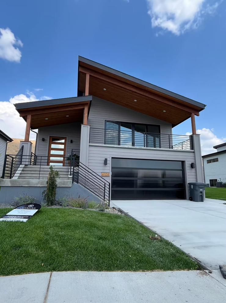 Modern two-story house with a sloped roof, garage, front stairs, and green lawn under a blue sky