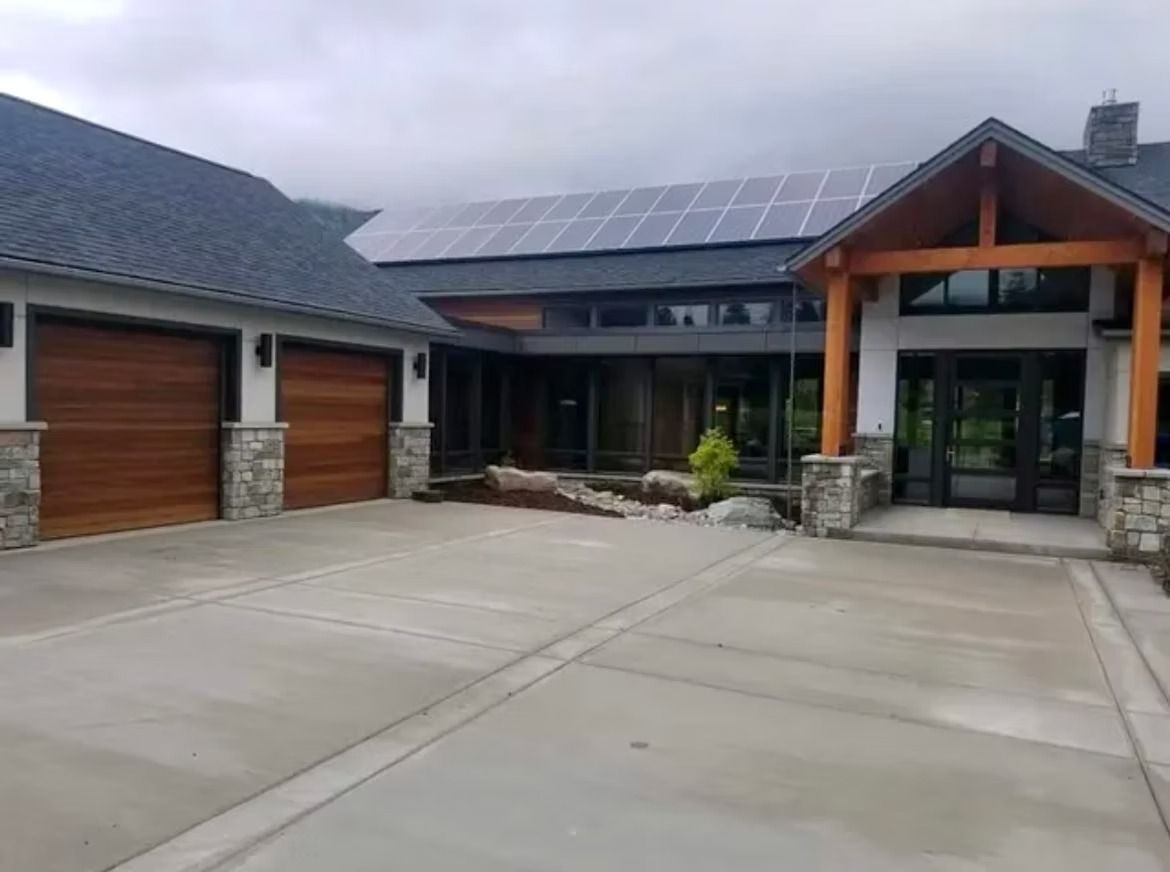 Modern house exterior with solar panels, concrete driveway, and wooden garage doors