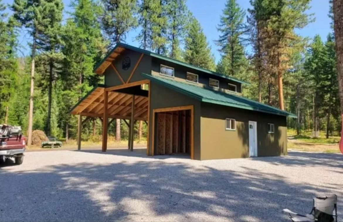 Modern cabin with green roof and covered porch in a wooded gravel lot