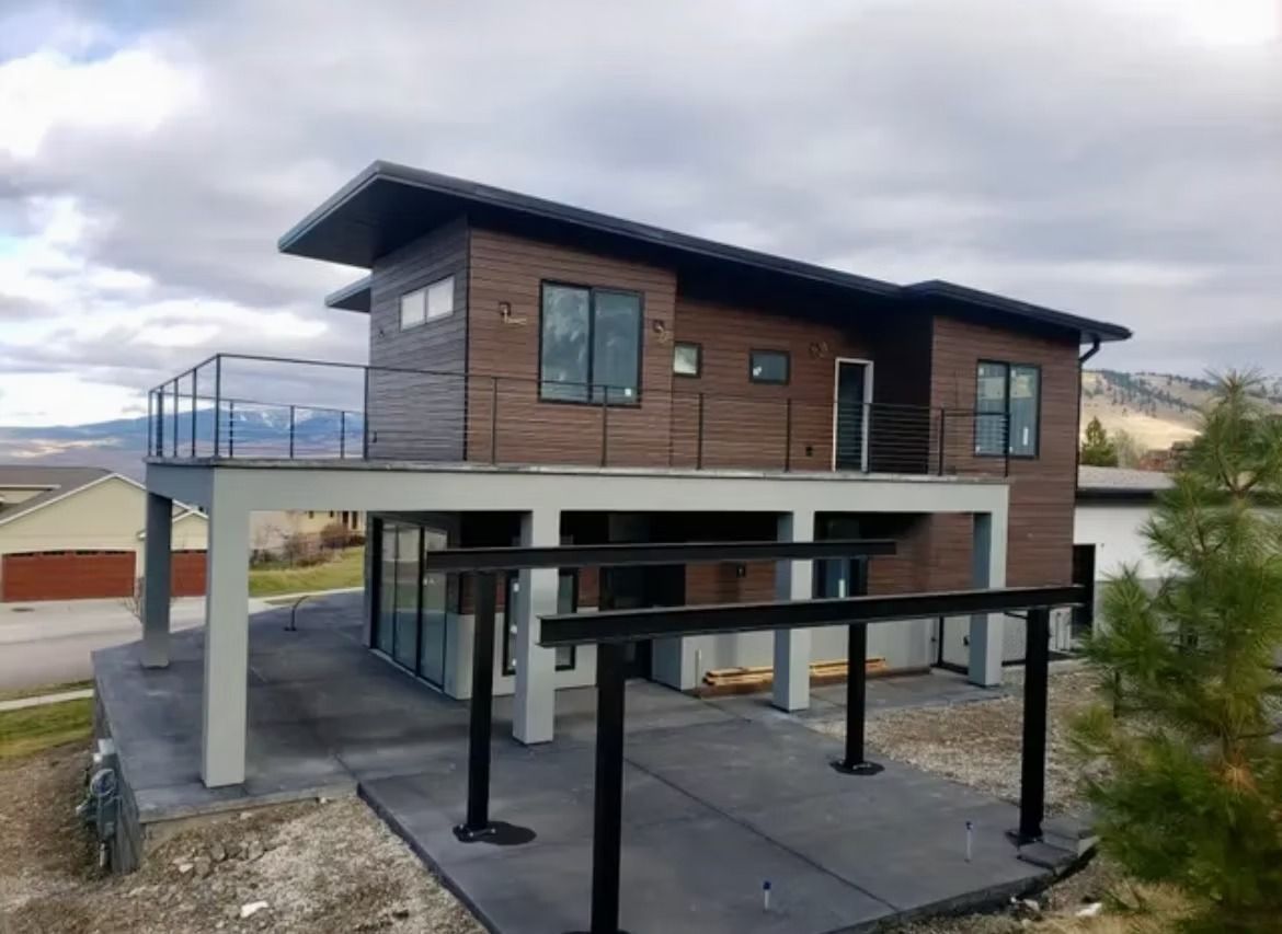 Modern two-story house with raised deck, dark siding, and black pergola on a cloudy day