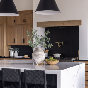 Modern kitchen with marble island, black pendant lights, wood cabinets, and a vase of greenery