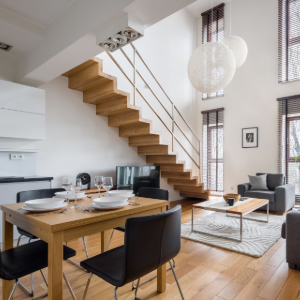 Modern open-plan dining and living room with wooden staircase, high ceilings, and large hanging pendant lights