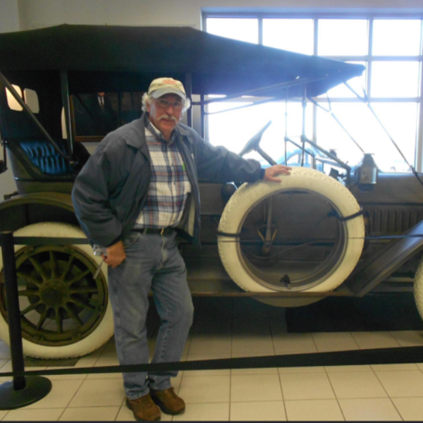 A man stands in front of an old car